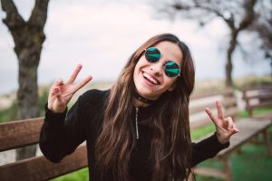 Portrait of young woman wearing mirrored sunglasses showing victory signs